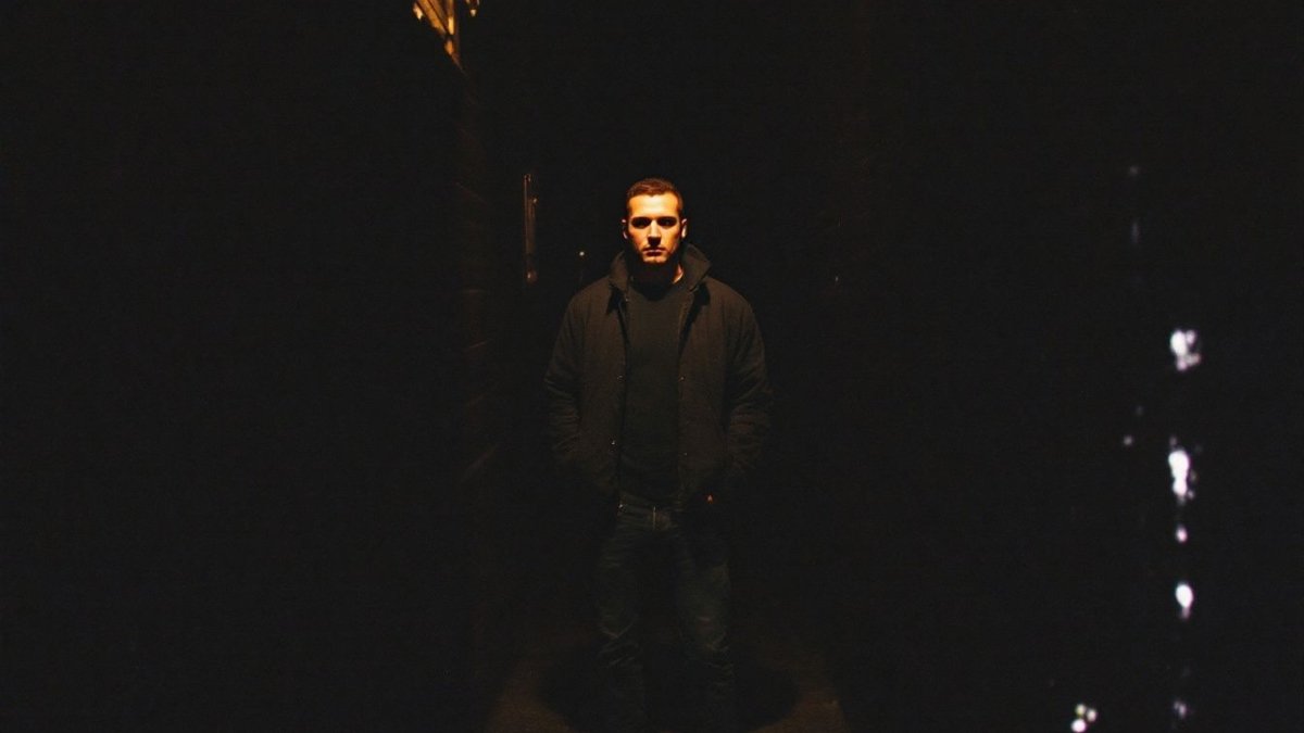 A figure standing in a dimly lit city alley.