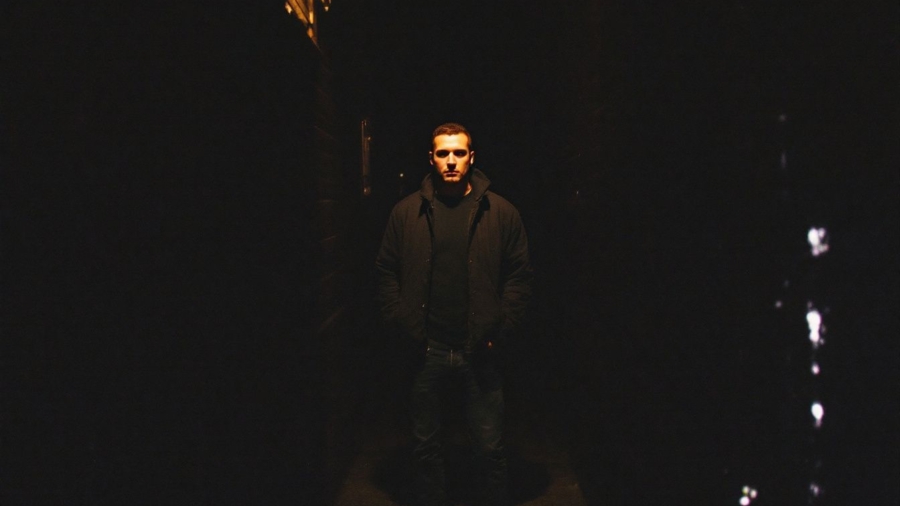 A figure standing in a dimly lit city alley.
